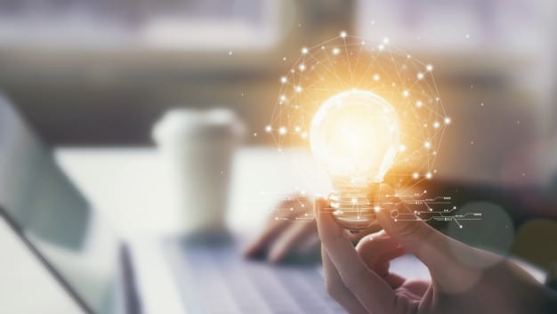 hand holding a bulb while working on a laptop